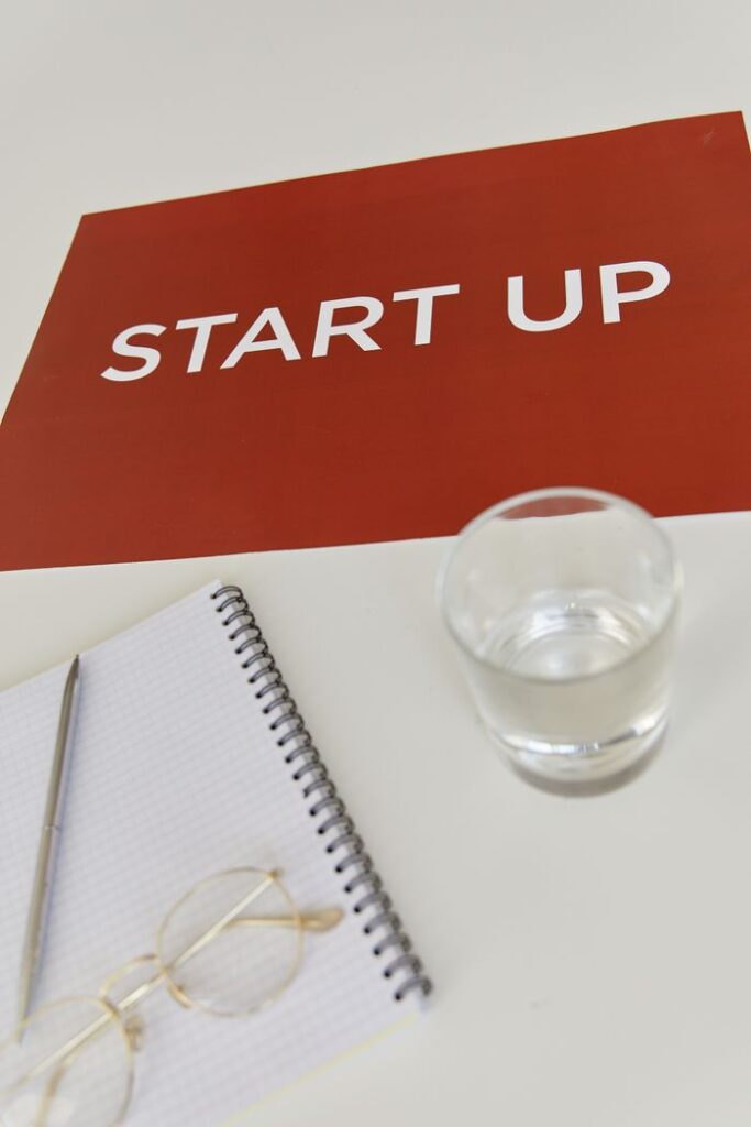 A modern workspace featuring a red 'Start Up' poster, notebook, pen, and glass of water.
